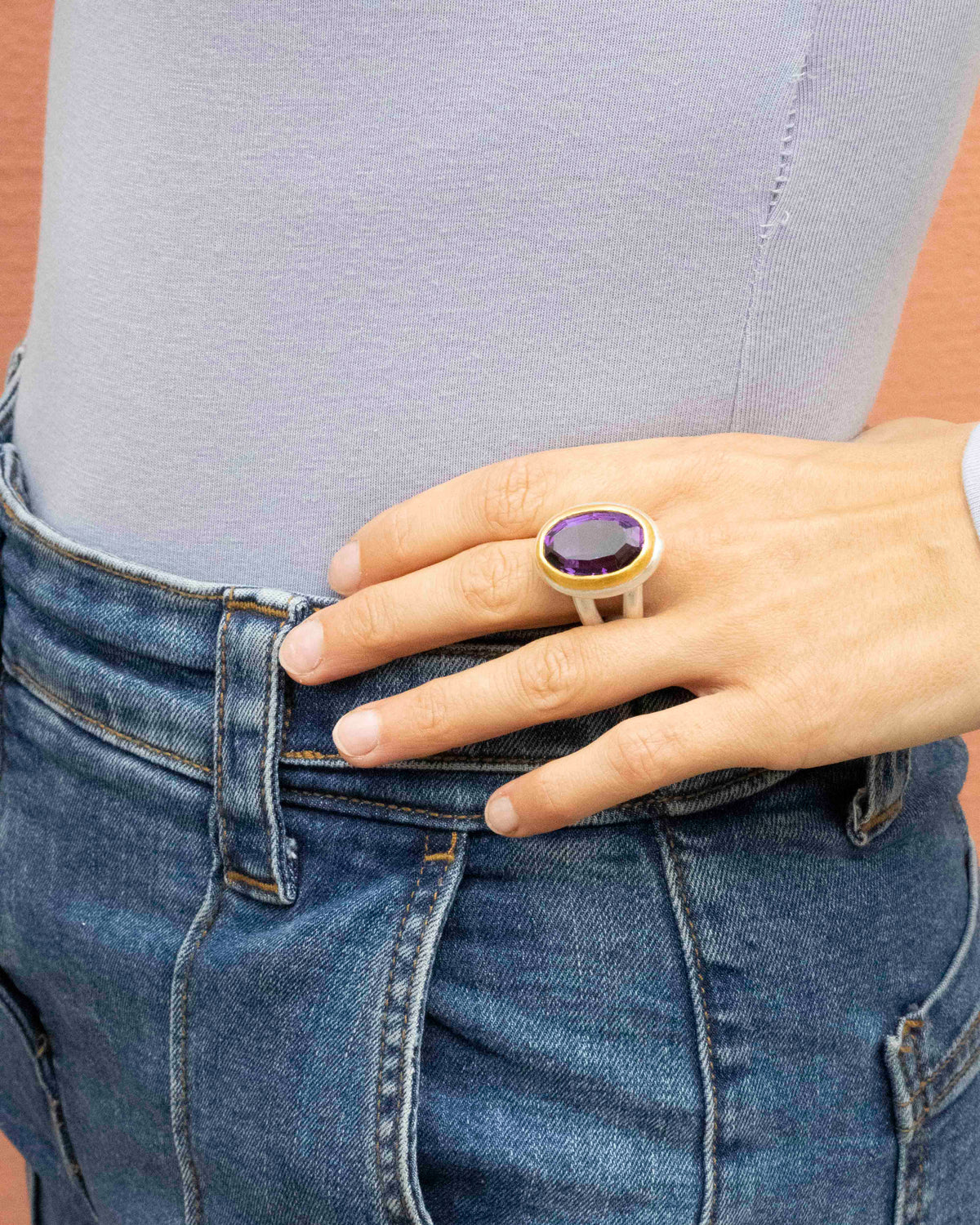 Facettierter Amethyst in Goldfassung auf Silberring, an der Hand einer Frau vor blauer Jeans