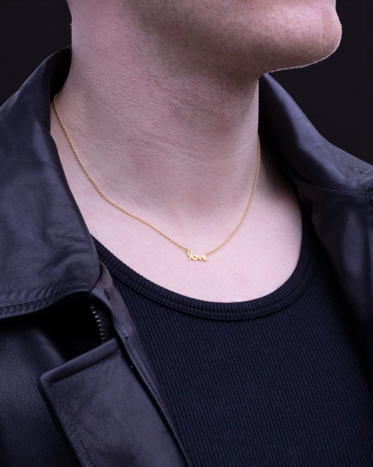Zarte Goldkette mit Love-Schriftzug am Hals eines Mannes mit schwarzer Lederjacke