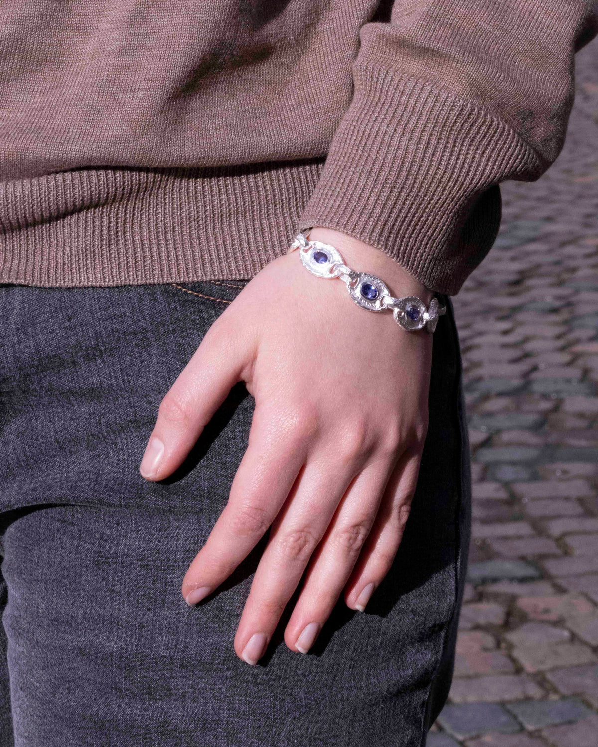 Silberarmband mit violettblauen Tansaniten am Handgelenk, altrosa Pullover und Kopfsteinpflaster