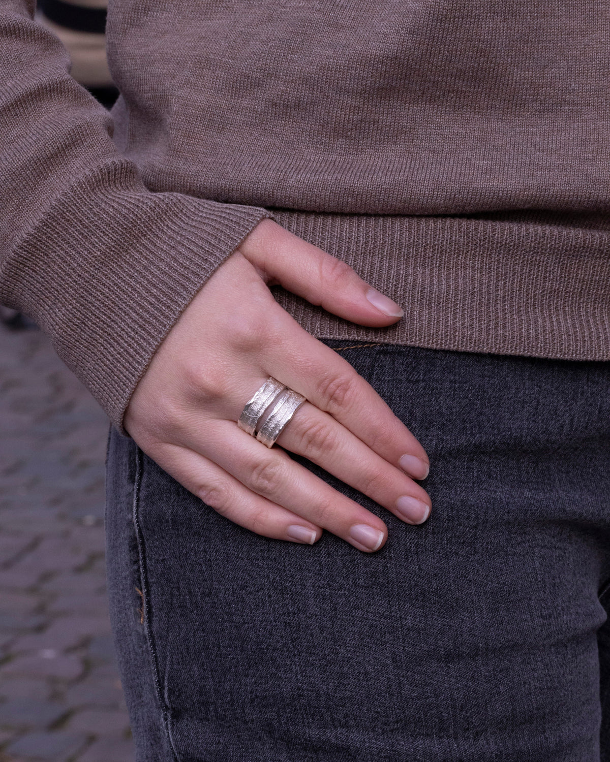 Breiter Silberring mit rauer Struktur und Spalt am Finger einer Frau, graue Jeans