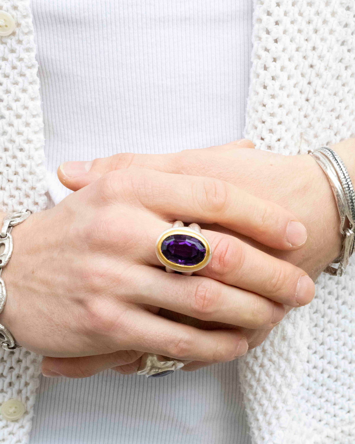 Silberring mit ovalem Amethyst in Goldfassung, getragen an der Hand vor weißer Strickjacke