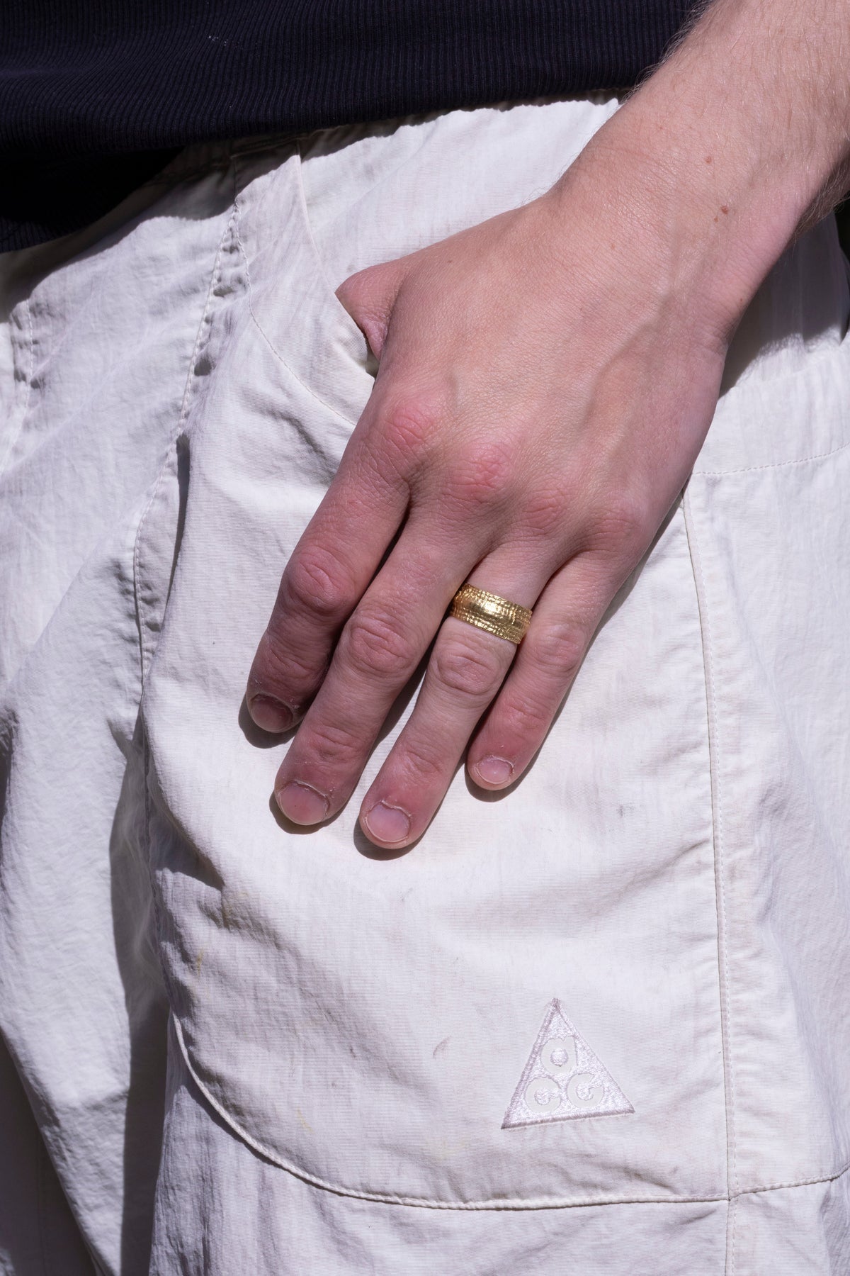 Massiver Goldring mit gehämmerter Nugget-Optik am Finger eines Mannes, Hand an heller Hose