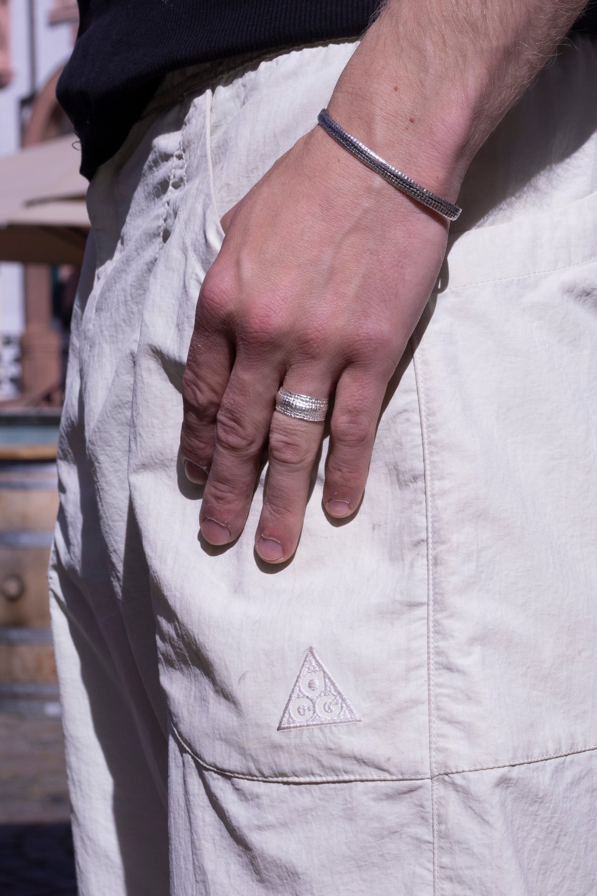 Silberner Bandring mit feiner Struktur am Finger eines Mannes, Silberarmband am Handgelenk