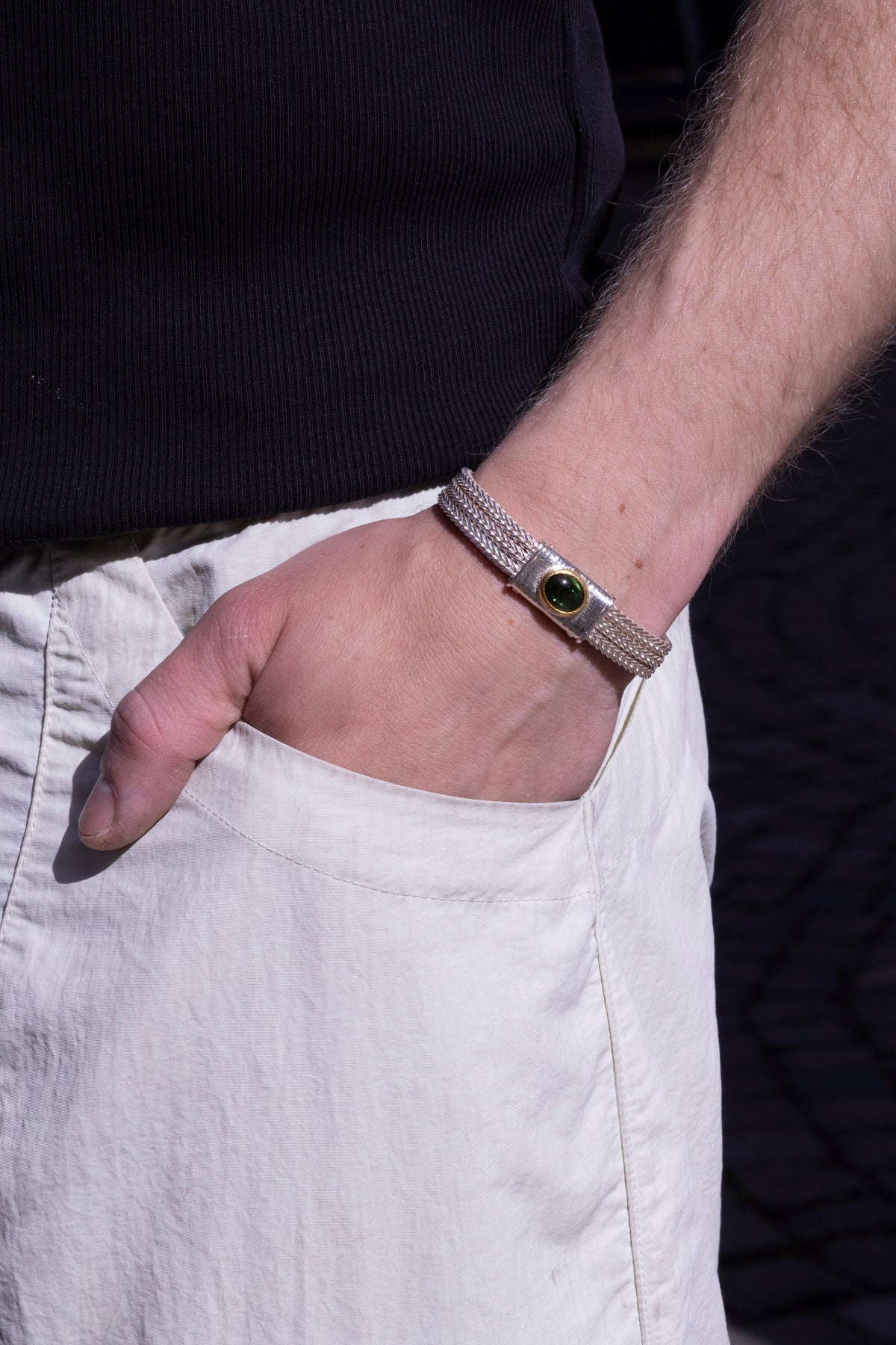 Geflochtenes Silberarmband mit grünem Turmalin am Handgelenk eines Mannes