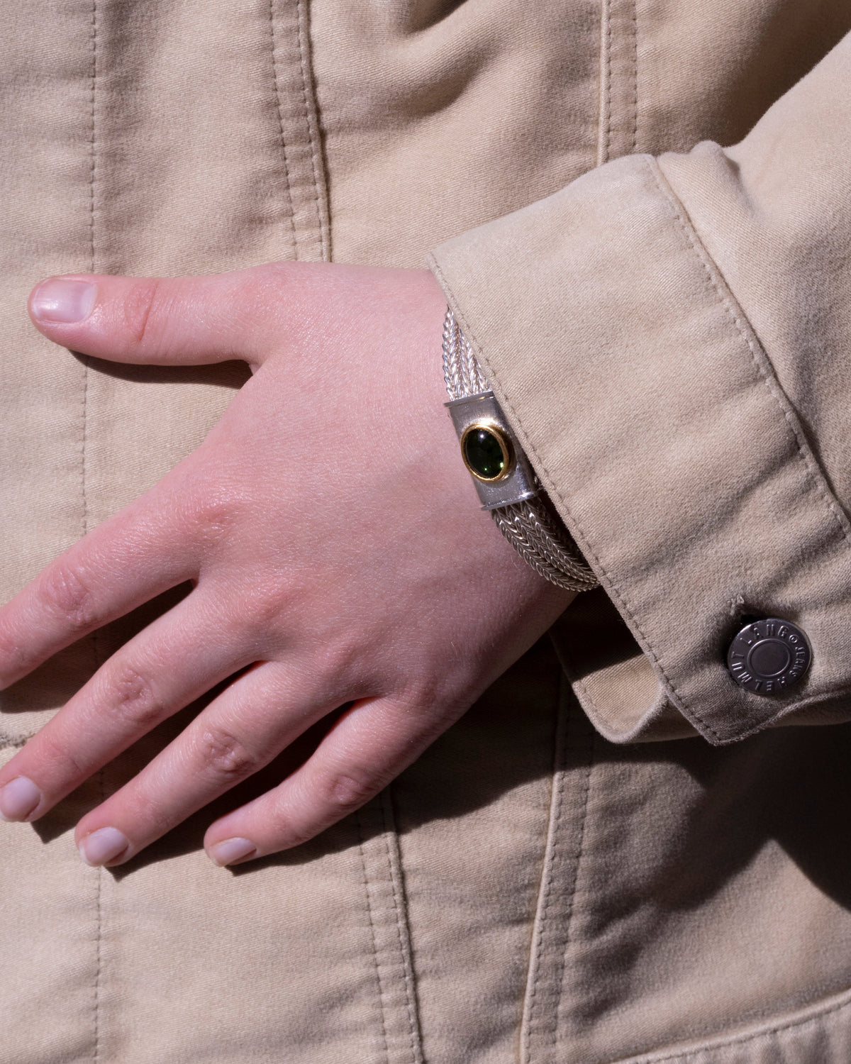 Silberarmband mit grünem Turmalin in Goldfassung am Handgelenk einer Frau, beige Jacke