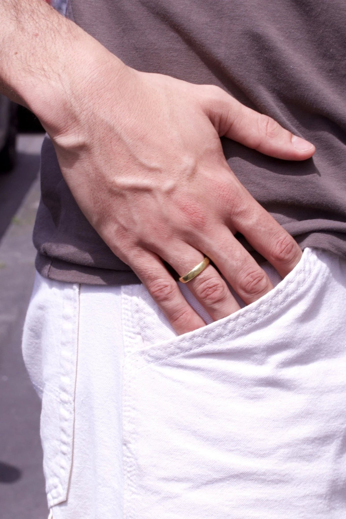 Matter Goldtrauring am Finger eines Mannes, Hand lässig in weißer Hosentasche
