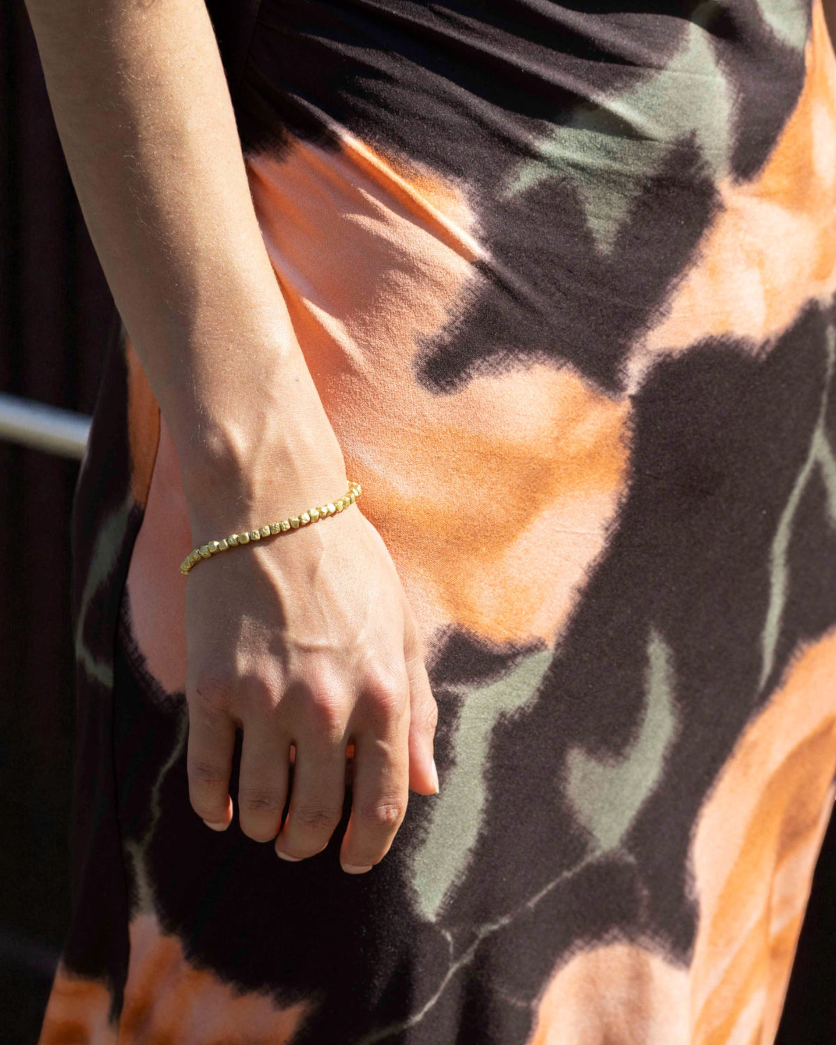 Nugget-Armband aus Gelbgold am Arm einer Frau, Batikkleid in Orange und Schwarz