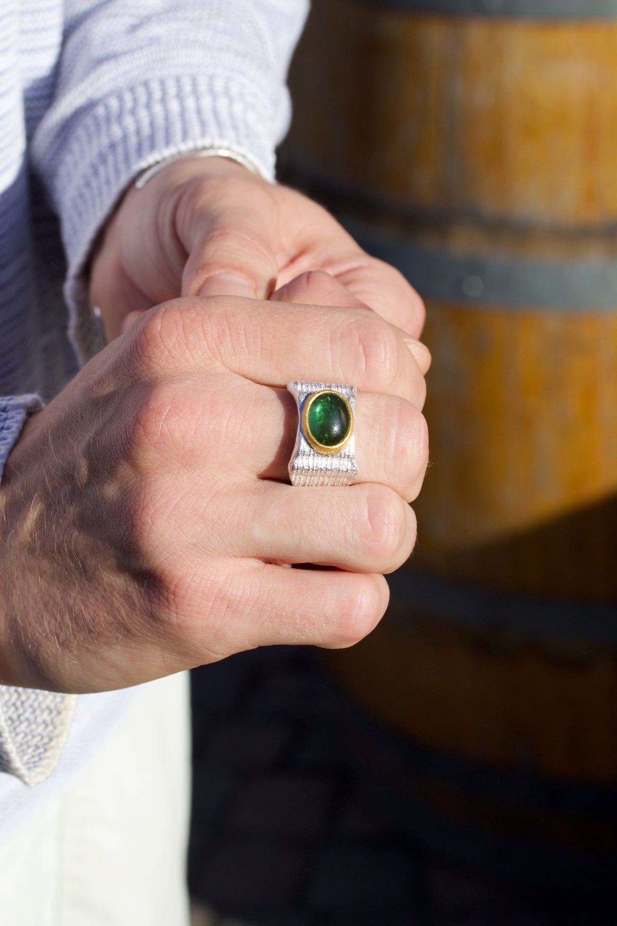 Ring aus 925 Silber mit grünem Turmalin, an der Hand getragen vor einem Weinfass
